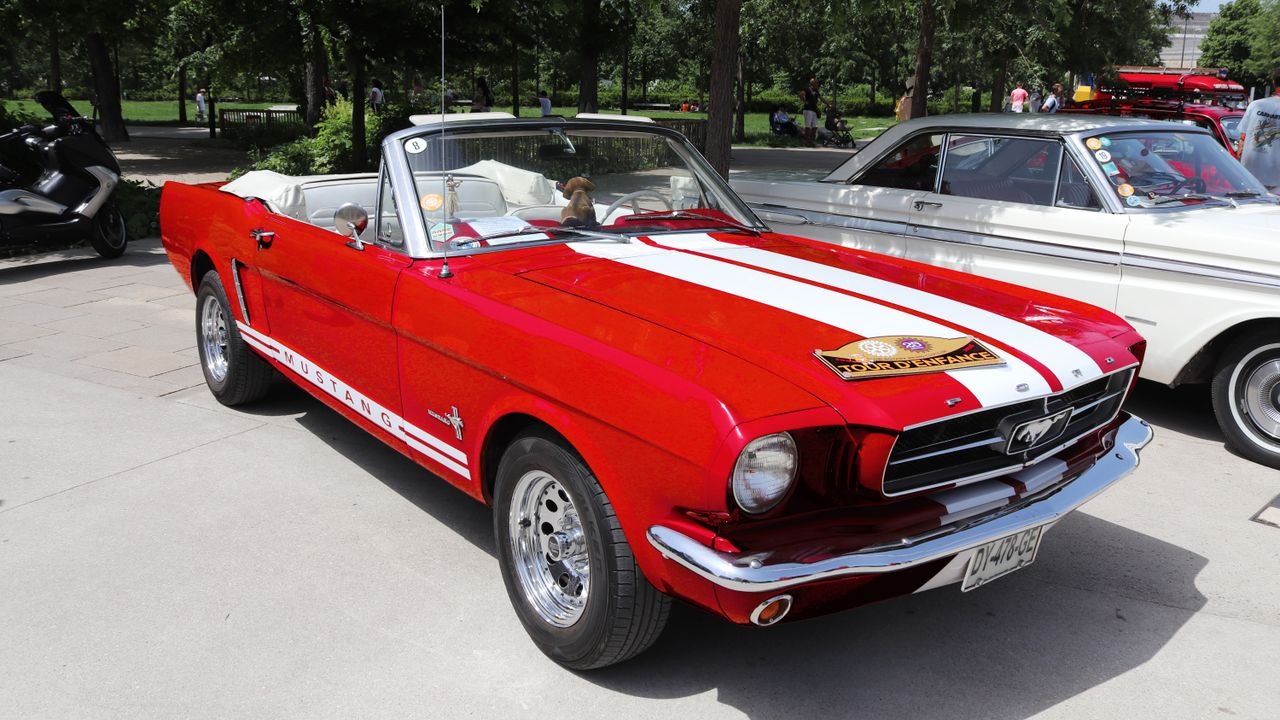 Vintage red Ford Mustang convertible with white stripes on display at an outdoor car show.